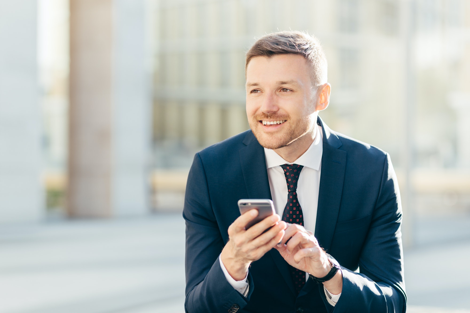 Delighted thoughtful elegant male marketing trader in formal black suit, uses modern cell phone
