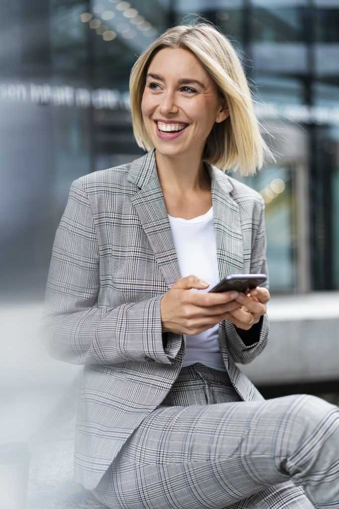Happy young businesswoman with mobile phone in the city
